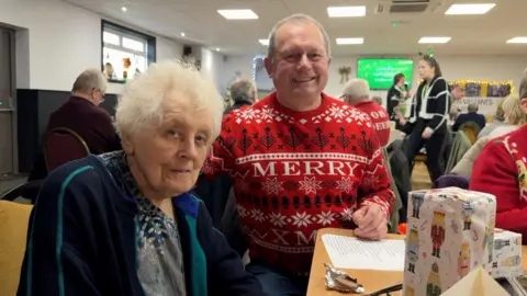 David Mason's mother, in blue, next to her son, who is wearing a Christmas jumper. Other people are in the background.