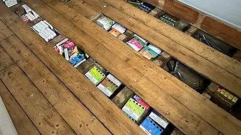 Dozens of boxes of vapes in bright packaging hidden under floorboards.