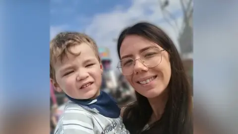 Emma Houston A woman with brown hair and glasses holding a toddler.