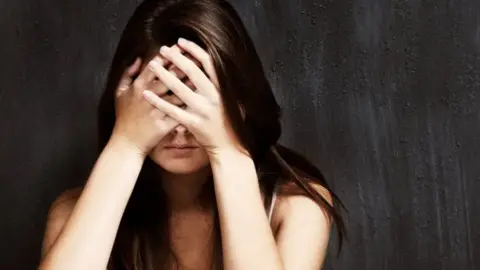 Woman with long brown hair sits covering her face 