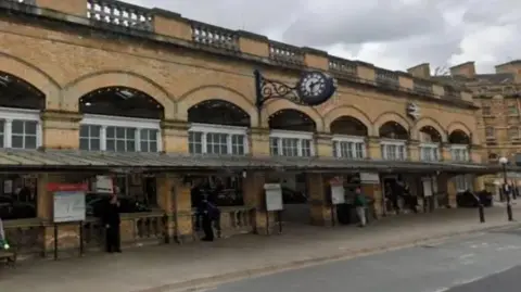 Google A light stone-built railway frontage bearing a large station clock fixed to the wall