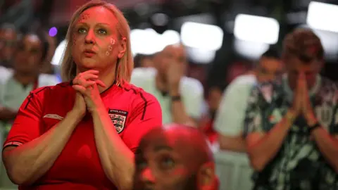 Getty Images An England fan in a red football shirt clasping her hands together with a tense, prayerful expression in a crowded venue.