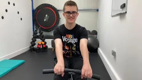 Alex Pope/BBC Zac Hollinshead, working out in a gym, on a rowing machine