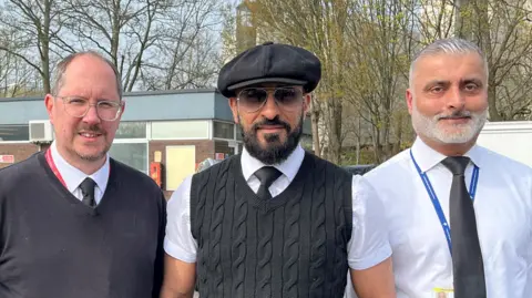 Mark, Arfan and Rahim stand side by side at the Gatwick Cars depot at the airport.