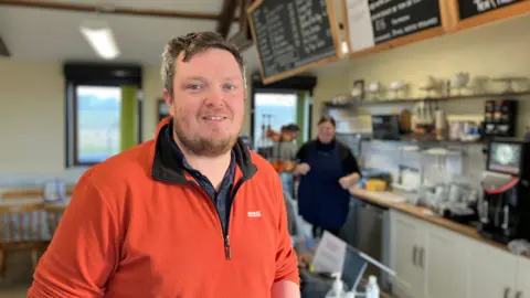 Ryan Dobson, manager at Watch Tree Nature Reserve, inside the cafe. He has short brown hair, blue eyes and a beard. He is wearing an orange fleece and looking at the camera.