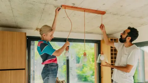 Getty Images Young woman and man adjusting hanging lights in a kitchen
