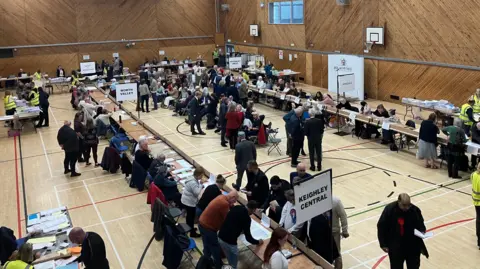 Grace Wood/BBC A hall full of people. The table layout and signage identifies it as an election vote count, in Keighley.