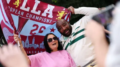 Getty Images Two Aston Villa fans clasp  a emblem  supra  them during the parade.