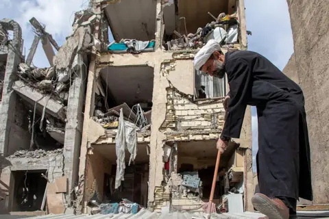 Getty Images A man sweeps up debris near a residential building that was hit in an airstrike in  in Tehran, Iran. 