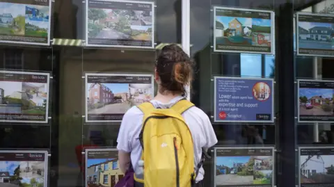 PA Woman looks at house adverts in a shop window