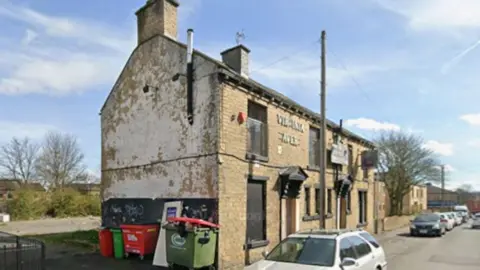 The former New Virginia Tavern on Rushton Road in Thornbury, a traditional pub with bins outside and cars parked on the street.