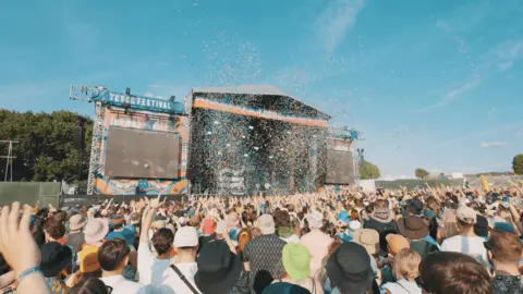 Harris Tomlinson-French Truck festival main stage. There are thousands of revellers in front of it and the sky is blue.