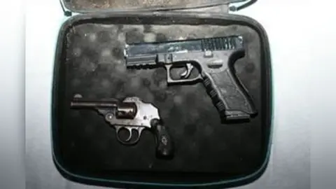 National Crime Agency Two guns - a Glock-style pistol and a small vintage-looking enclosed-hammer revolver - lie in a small case which has black padding.