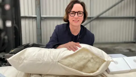 A woman with glasses and dark hair holds open a pillow with wool inside
