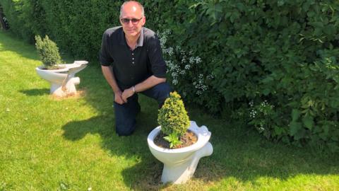 Andy Maddams with two toilet bowls filled with conifer trees