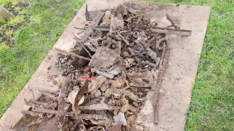 Mark Mather A metal panel laid down on the grass contains lots of metal objects and debris dug up from the park.