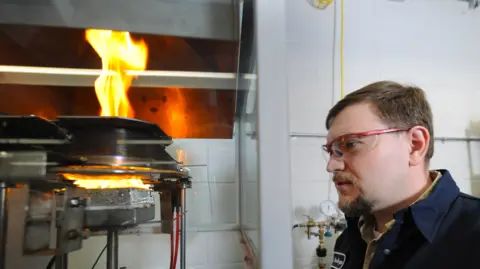 University of Dayton Research Institute Wearing safety specs Alex Morgan inspects a heat test which has a large flame burning. 