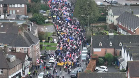 A group of protesters, many with Union Jack flags, marching down a street.