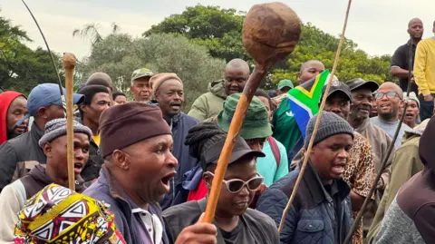 Thuthuka Zondi / BBC Protesters in Durban, some holding traditional weapons