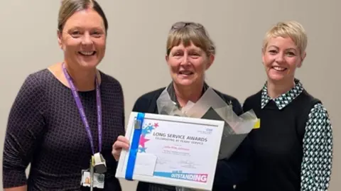 Northwest Anglia Foundation NHS Trust Oncology Clinical Nurse Specialist (centre) - J.J , a woman receiving 40 year service award from Chief Nurse Jo Bennis and Zara Ball, Lead Cancer Nurse 