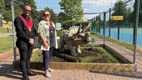 Warminster Town Council Two people stood next to a dinosaur in a cage.