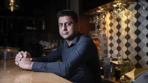 Zafar wearing a black shirt looking at the camera with his hands held together.