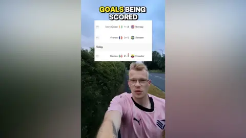 Tom Willmott Tom is wearing a pink top as he films himself running by a road. The goals and amount he has to run appear in a box over his head.