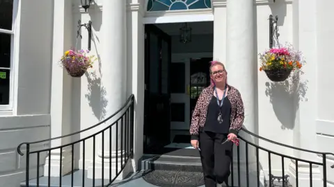 Jess Fry standing on steps in front of a white brick building
