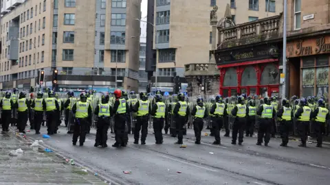 PA Media The view from behind of a row of police, most with shields, as Celtic fans take over the Trongate area of Glasgow to celebrate winning the league 