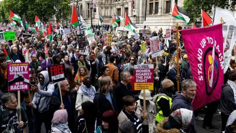 Getty Images At least 100 people are seen in a picture from a portion of the Nakba Anniversary march in London - about a dozen Palestinian flags can be seen in the background, as well as placards in the foreground that say things like 