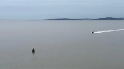 Bay Search and Rescue People stand huddled together, knee deep in water, as a speedboat races towards them.