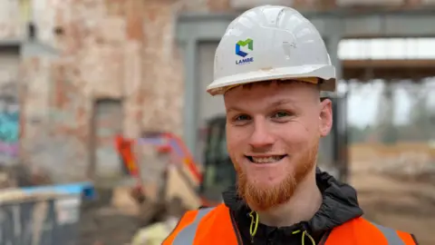 Young smiling man with a ginger beard in a white hard hat and orange hi-vis jacket