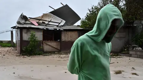 EPA A man in a green hoodie walks past a damaged property in Jamaica 