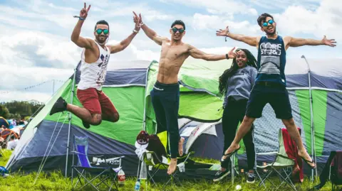 Creamfields Three men and one woman jumping and smiling at the camera outside a tent at the camping site at Creamfields.
