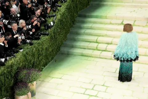 MG26/Getty Images for The Met Museum/Vogue Anna Wintour attends The 2026 Met Gala Celebrating "Costume Art" at the Metropolitan Museum of Art on May 04, 2026 in New York City. Wintour wears her hair in her signature bob and sports dark sunglasses. Her dress is an avian-inspired confection, with a turquoise feathered cape on top of a darker-green dress whose embroidery resembles feathers.