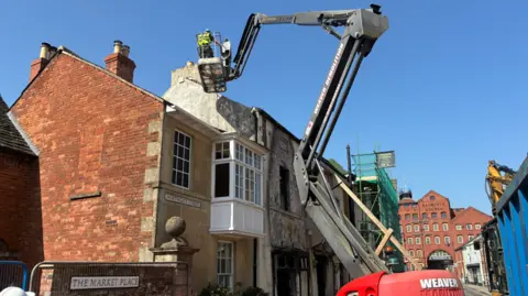 A man in high-vis on a cherry picker which looms over a fire-hit building.