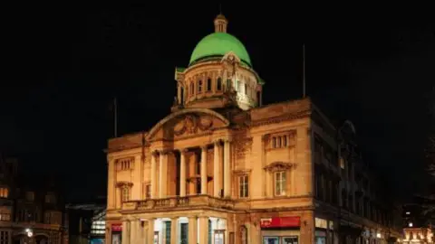 Hull City Hall - a grand historic building in the centre of Hull. It is lit up in a yellow colour. 