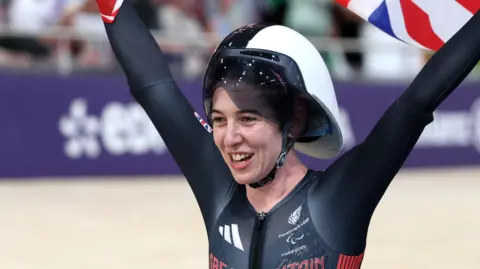 Great Britain paracylist Sophie Unwin celebrates by flying the Union Jack behind her head she cycles around a velodrome after taking Gold at the 2024 Olympic Games in Paris