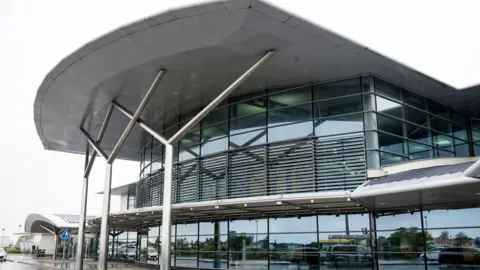 The Guernsey Airport terminal with a number of pylons holding up a roof with glass windows. 