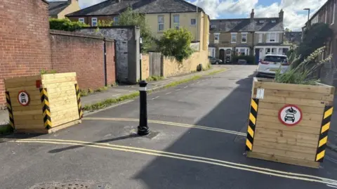 LTN planters and bollards on an Oxfordshire street. It's a sunny day.