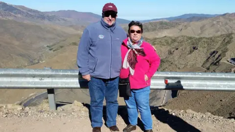 Contributed Rodrick Lodge and his woman  Pauline lasting  successful  beforehand   of a mountainous landscape. They are some  wearing fleeces and sunglasses and smiling astatine  the camera. 