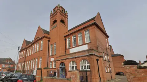 A large redbrick Victorian former school building with a bell tower