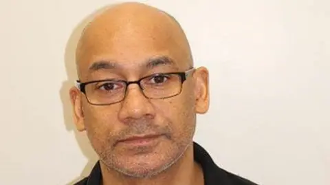 Met Police Trevor Gocan, 57, in a dark coloured polo t-shirt. He wears glasses.