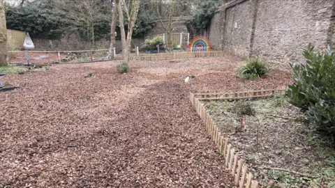 Jade Hoskin A view of the memorial garden. It has wood chip on the ground, a rainbow in the right corner and a small area in the front right.