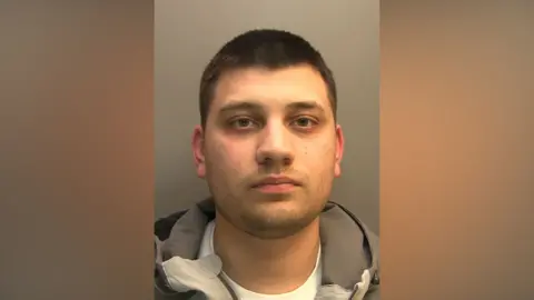 Lincolnshire Police Police custody photograph of Ethan Taylor he has short black hair and beard and is wearing a grey jacket and white shirt