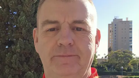 Robert Martin Secretary of Derry City football club Robert Martin has short brown hair and is wearing a Derry City shirt near a city skyline. 