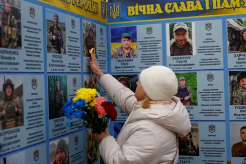 Reuters A woman touches a portrait of her relative while she visits a memorial dedicated to fallen Ukrainians on the fourth anniversary of Russia's full-scale invasion, in Kyiv, Ukraine.