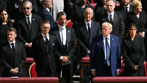 Getty Images US President Donald Trump (C) and First Lady Melania Trump stand alongside French President Emanuel Macron (left)