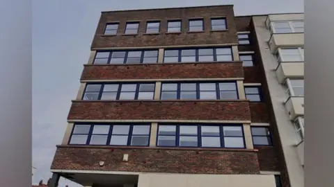 A brown block of flats, four stories high.