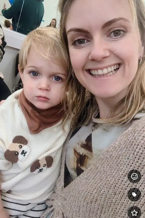 Mari Ellis Dunning A woman with long blonde hair is smiling while holding a little boy with short blonde hair.